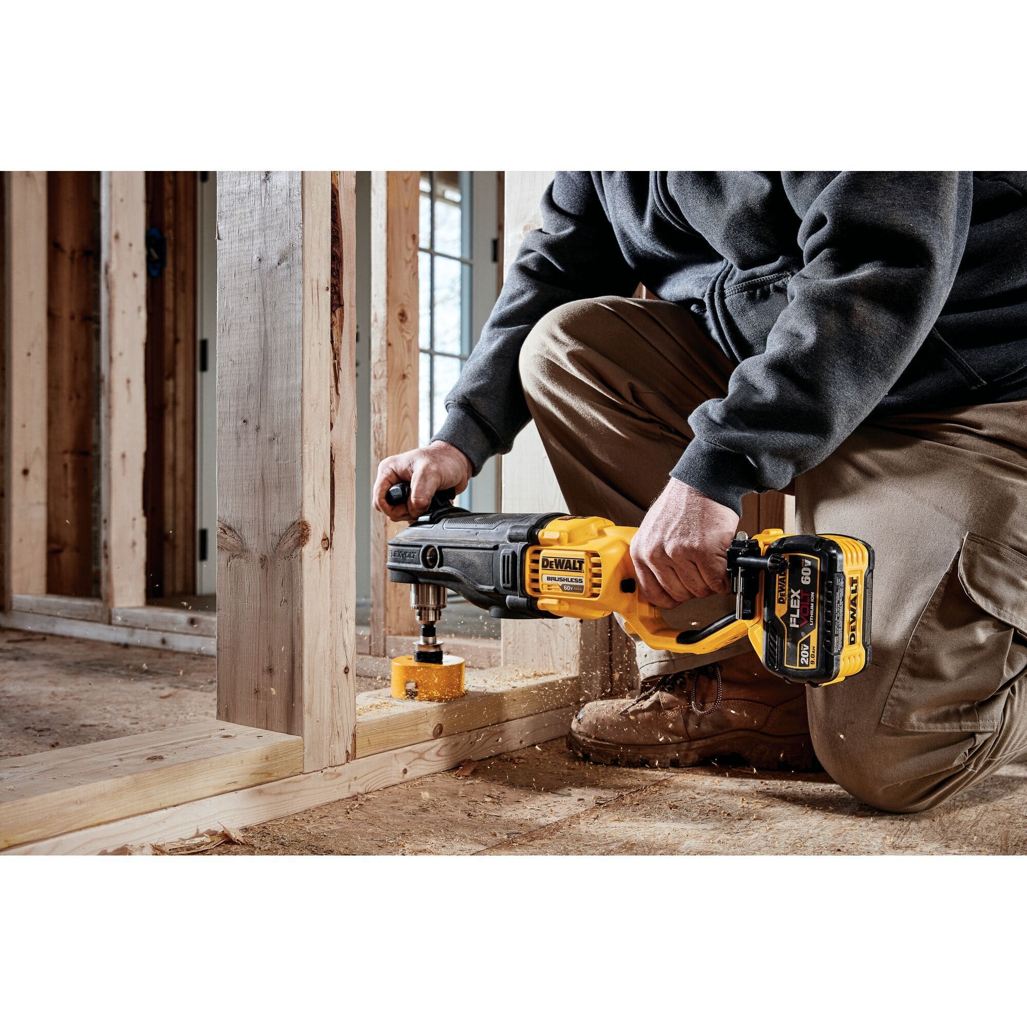 Contractor in a wooden framing environment using the DEWALT DCD470X1 cordless stud and joist drill equipped with a large hole saw to effortlessly cut through a vertical wood stud for plumbing or electrical lines.