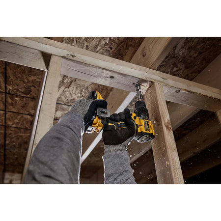 Action shot of a professional using the DEWALT ATOMIC hammer drill to drive a hole through a wooden ceiling joist in a residential framing environment, demonstrating overhead maneuverability.