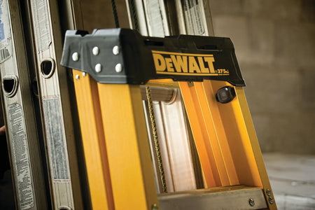 An action shot of the DEWALT DCE041 Bluetooth tag securely mounted to the side rail of a yellow fiberglass step ladder. The small, discreet profile of the tag is shown, illustrating how it can be placed inconspicuously on large jobsite assets to prevent theft and aid in inventory identification.