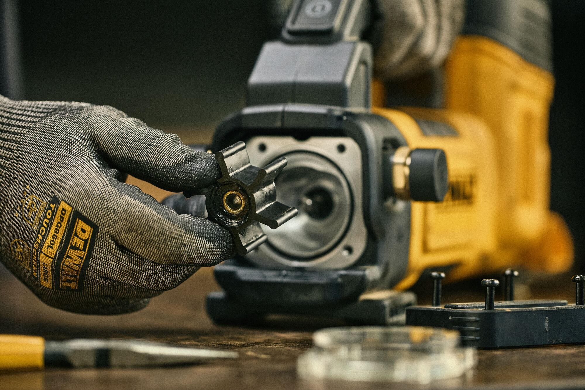 Full jobsite view of a construction worker or plumber inserting a 20V MAX battery into a DEWALT 10 GPM cordless transfer pump placed on a blue barrel inside a utility van filled with hoses and copper pipes.