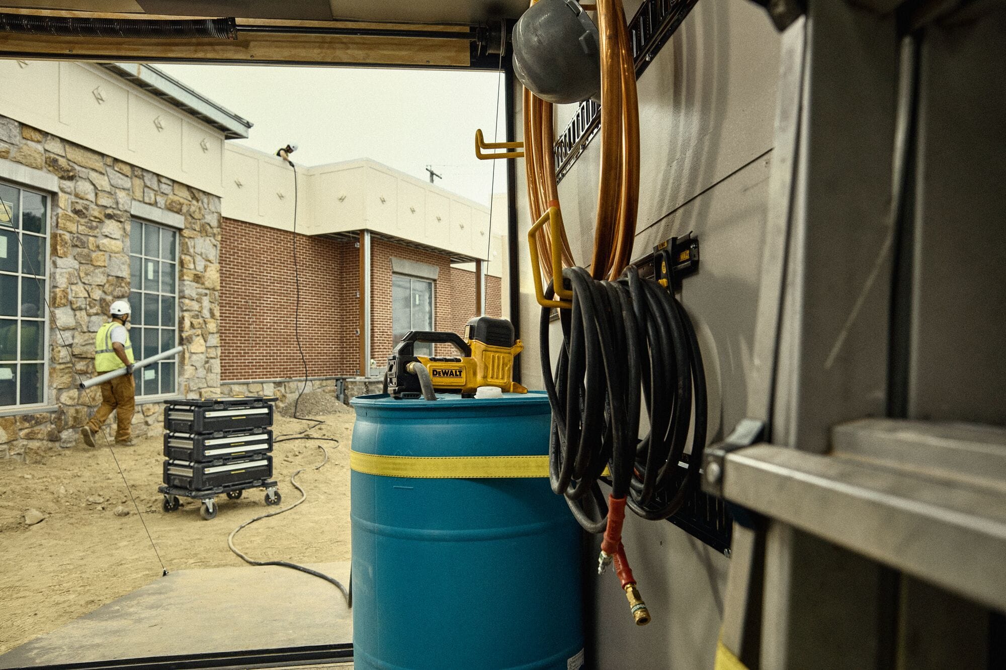 Close-up photograph of a worker wearing DEWALT protective gloves pulling a flexible rubber impeller out of the pump chamber of a DCE050 cordless transfer pump on a workshop table for routine tool maintenance.