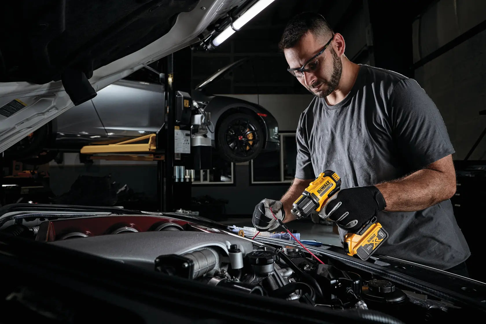 Professional technician using the DEWALT 20V MAX cordless heat gun to apply shrink tubing to automotive wiring under the hood of a car.