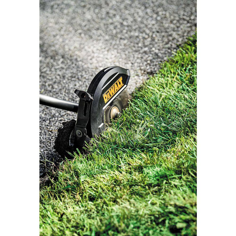 Close-up action shot of the DEWALT DCED472B 7.5-inch hardened steel blade cutting thick grass overgrowth to create a crisp commercial landscaping edge along a paved border.