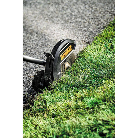 Close-up action shot of the DEWALT DCED472B 7.5-inch hardened steel blade cutting thick grass overgrowth to create a crisp commercial landscaping edge along a paved border.