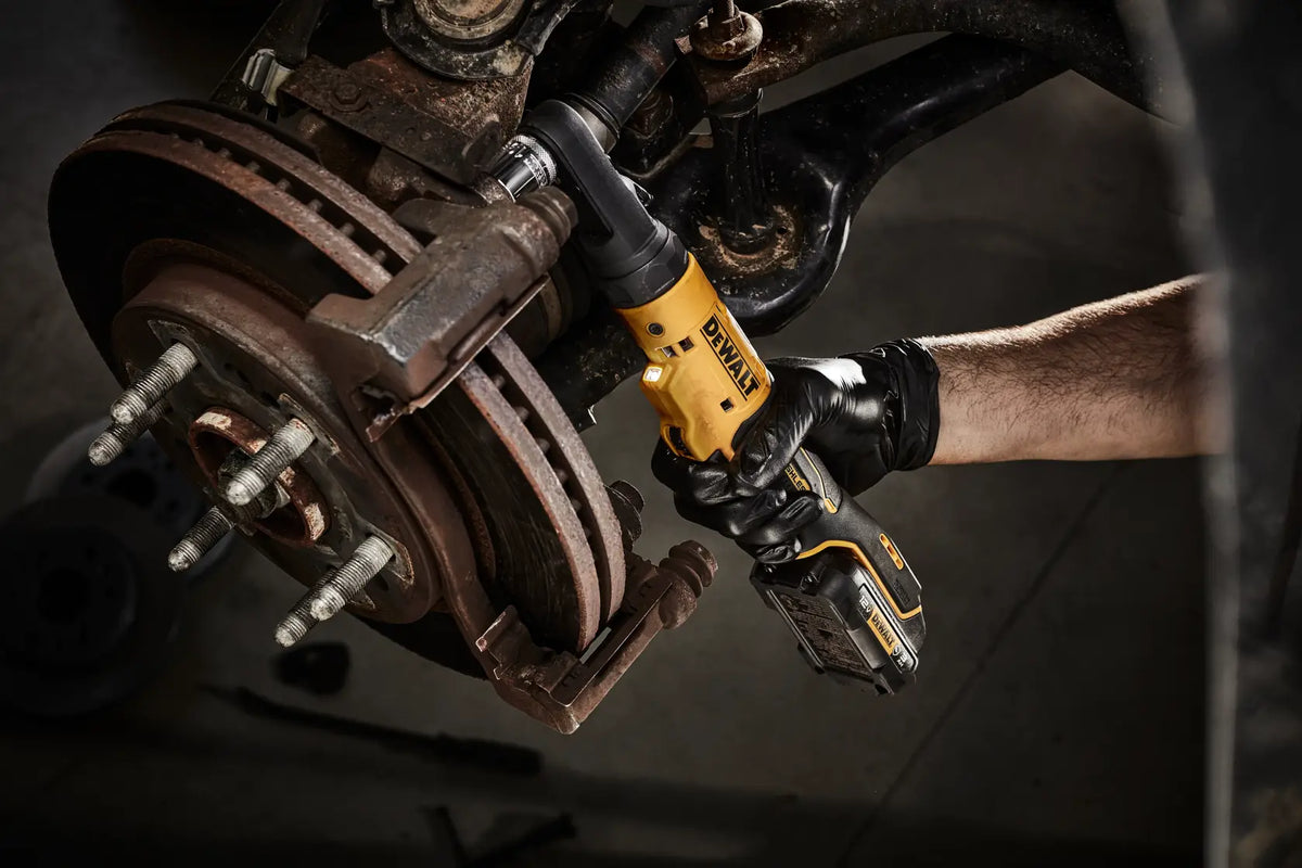 Close-up of the DEWALT 12V MAX brushless ratchet being used on a brake rotor assembly, illustrating the precision and visibility provided by the integrated LED light in dark mechanical areas.