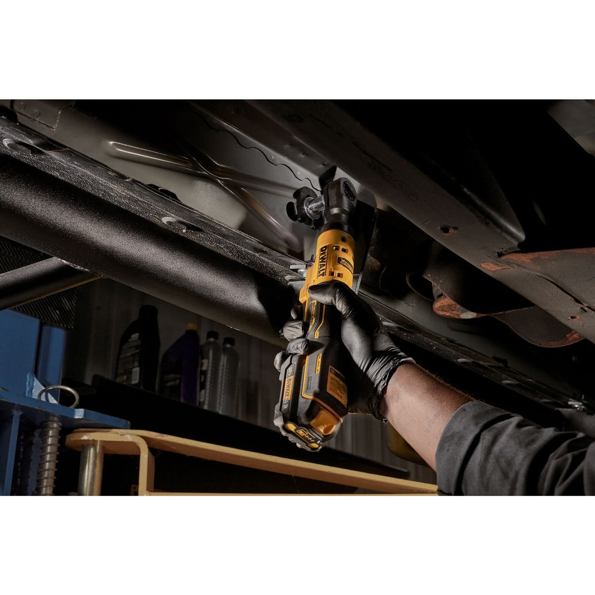 Professional mechanic operating the DEWALT DCF503B XTREME cordless ratchet from beneath a vehicle, demonstrating the tool's high-torque capability and ergonomic reach.