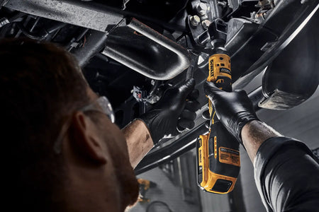 Professional mechanic utilizing the compact DEWALT 20V MAX brushless 1/2-inch cordless ratchet alongside a hand wrench to efficiently tighten suspension bolts in a tight automotive workspace.