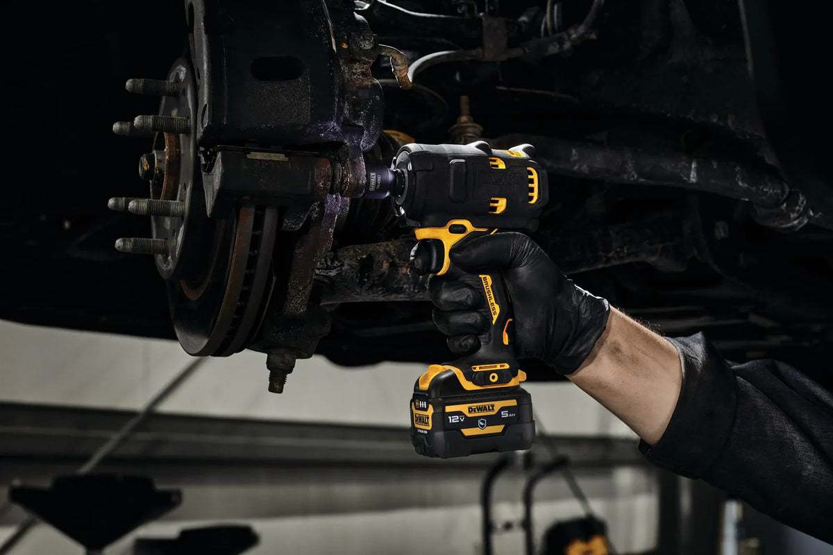 Professional mechanic wearing black nitrile gloves using the DEWALT DCF901B XTREME 12V MAX brushless 1/2-inch cordless impact wrench to remove a heavy-duty bolt from a vehicle brake assembly.