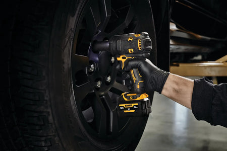 Action shot of an automotive technician utilizing the DEWALT 12V MAX brushless impact wrench to fasten lug nuts on a black custom truck wheel, demonstrating high-torque performance in a garage setting.
