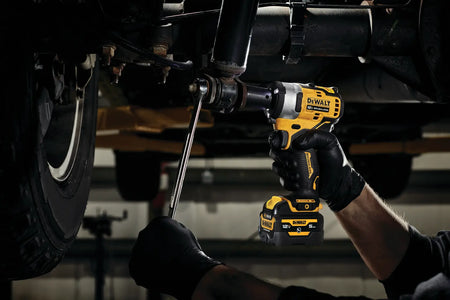 Technician using the DEWALT 12V MAX brushless 1/2-inch impact wrench to perform maintenance on a vehicle's shock absorber in a professional garage setting.
