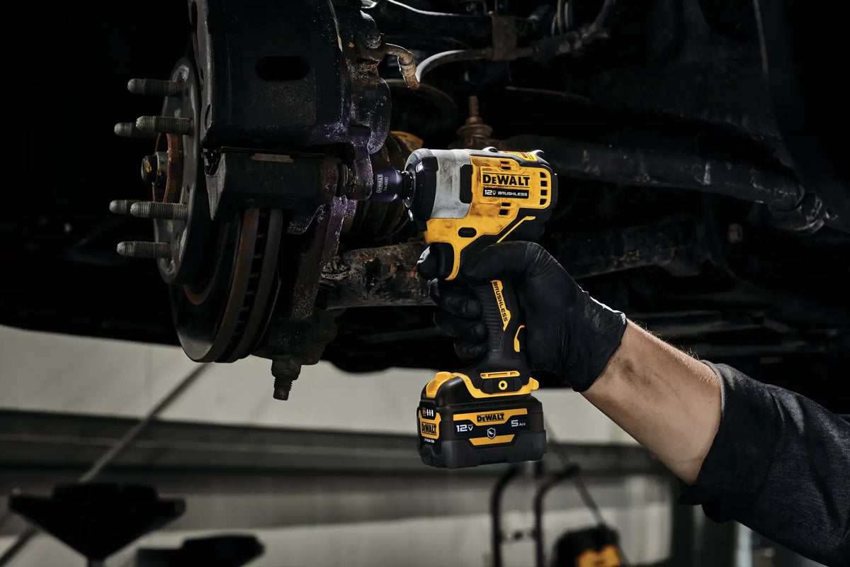 View of an electrician or mechanic using the DEWALT XTREME sub-compact impact wrench to remove fasteners from a large brake rotor assembly on a vehicle lift.