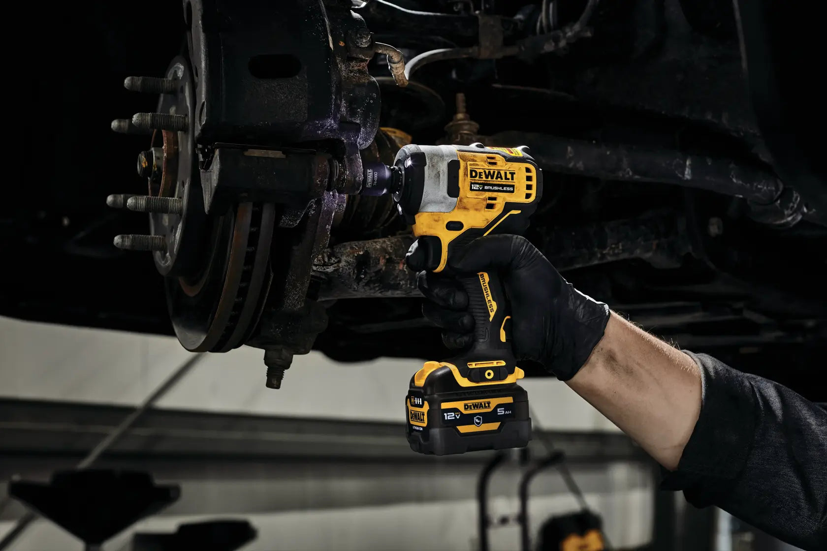 View of an electrician or mechanic using the DEWALT XTREME sub-compact impact wrench to remove fasteners from a large brake rotor assembly on a vehicle lift.