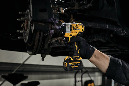 View of an electrician or mechanic using the DEWALT XTREME sub-compact impact wrench to remove fasteners from a large brake rotor assembly on a vehicle lift.
