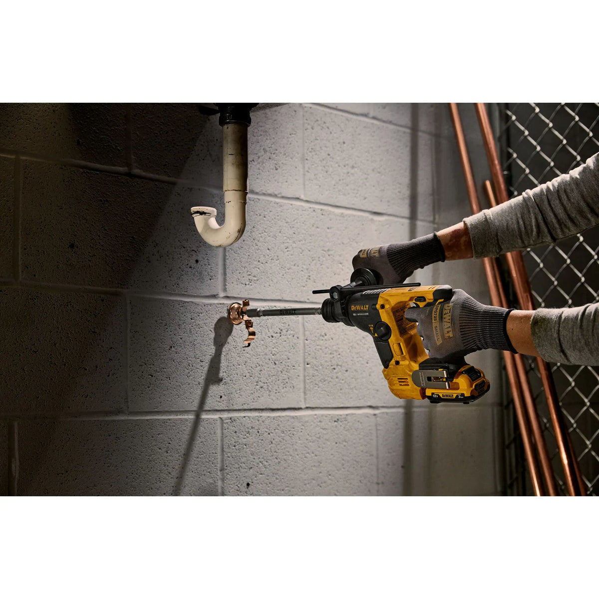 Action shot of the DEWALT XTREME sub-compact rotary hammer being used in a confined space to install a pipe clamp anchor into a masonry wall.