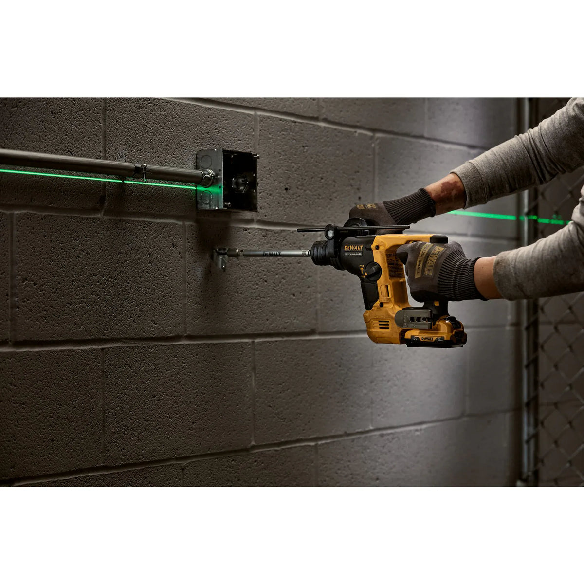 An ironworker using the DEWALT DCH072B 12V MAX rotary hammer to drill an anchor hole into a masonry wall, with a green self-leveling laser line providing a horizontal reference.