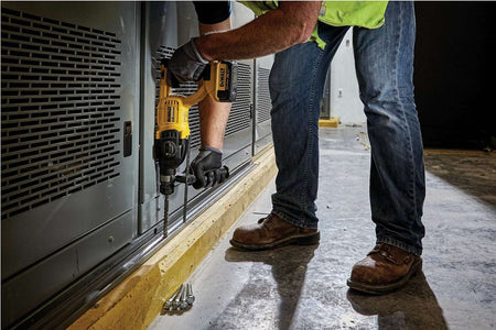 Jobsite application showing a professional worker using the DEWALT D-handle SDS Plus rotary hammer to drill precise holes into a concrete floor for heavy-duty fastener installation near industrial equipment.