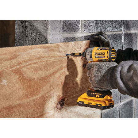 Action shot of a contractor using the DEWALT 20V MAX brushless impact driver to drive a fastener into a wood panel against a concrete block wall in a construction environment.