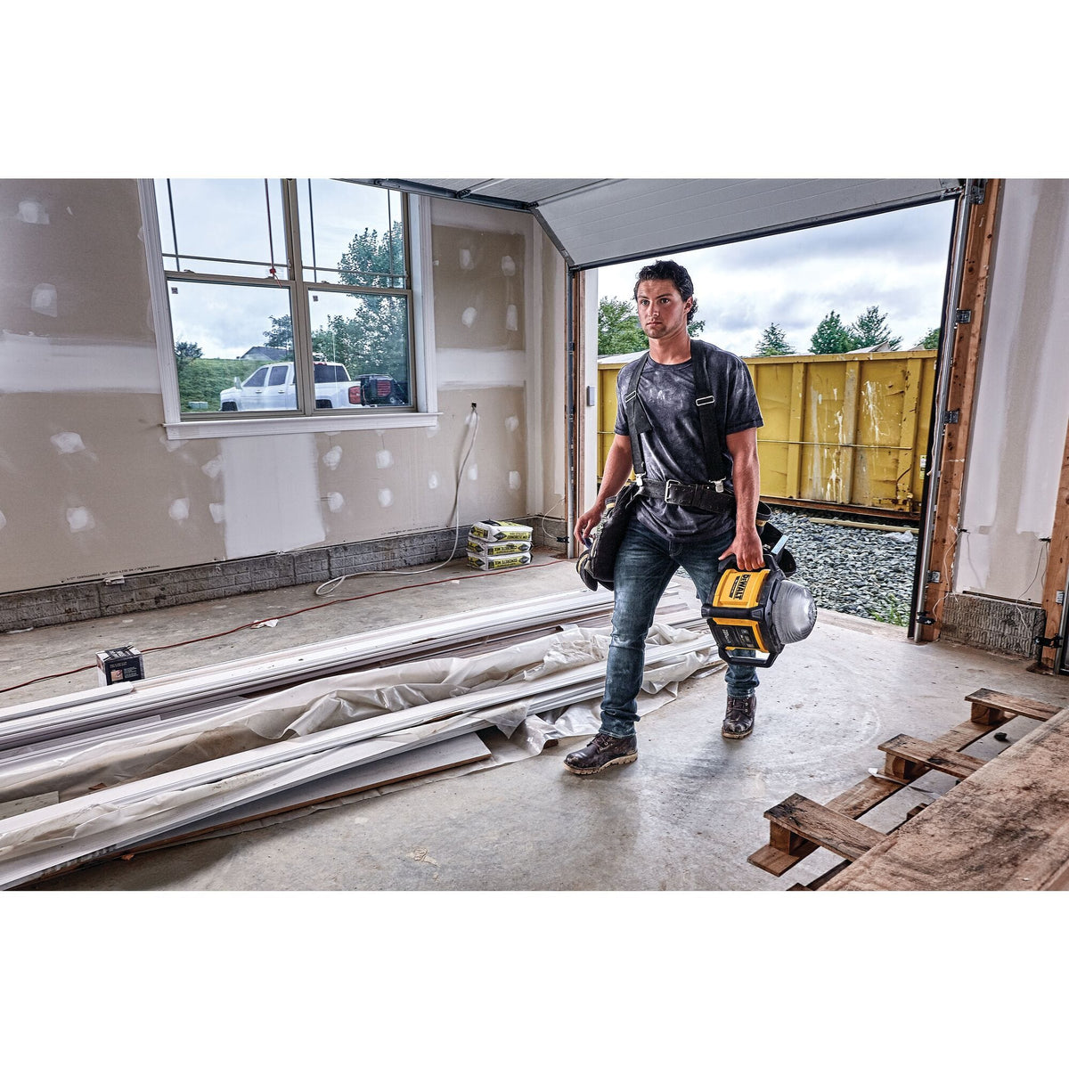 A professional tradesperson carrying the compact and portable DEWALT DCL074 LED work light through an active residential construction site for quick and easy jobsite setup.