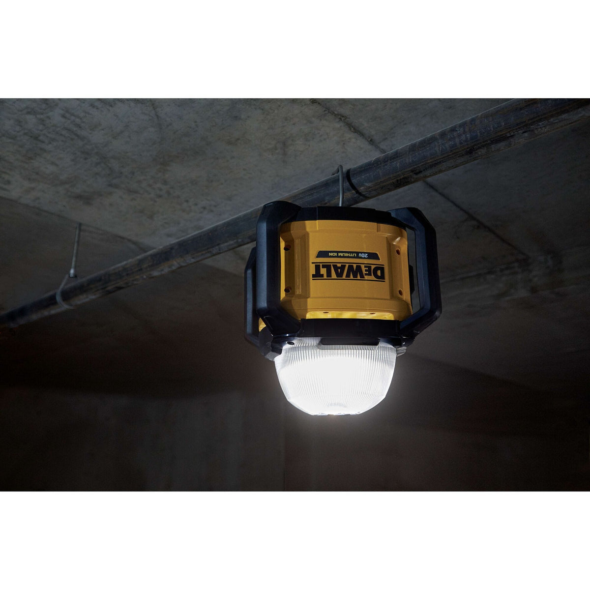 Close-up shot of the DEWALT DCL074 LED work light suspended upside down from a ceiling pipe using its integrated heavy-duty hanging hook, highlighting its versatile mounting options for jobsite lighting.