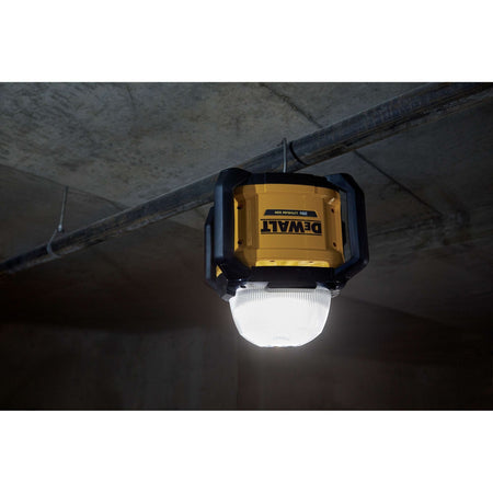 Close-up shot of the DEWALT DCL074 LED work light suspended upside down from a ceiling pipe using its integrated heavy-duty hanging hook, highlighting its versatile mounting options for jobsite lighting.