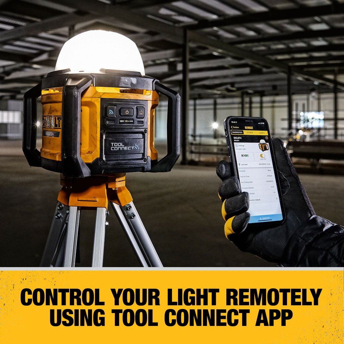 An operator using a smartphone to remotely manage the DEWALT DCL074 work light via the Tool Connect app while the unit is mounted on a tripod in a large-scale commercial workspace.