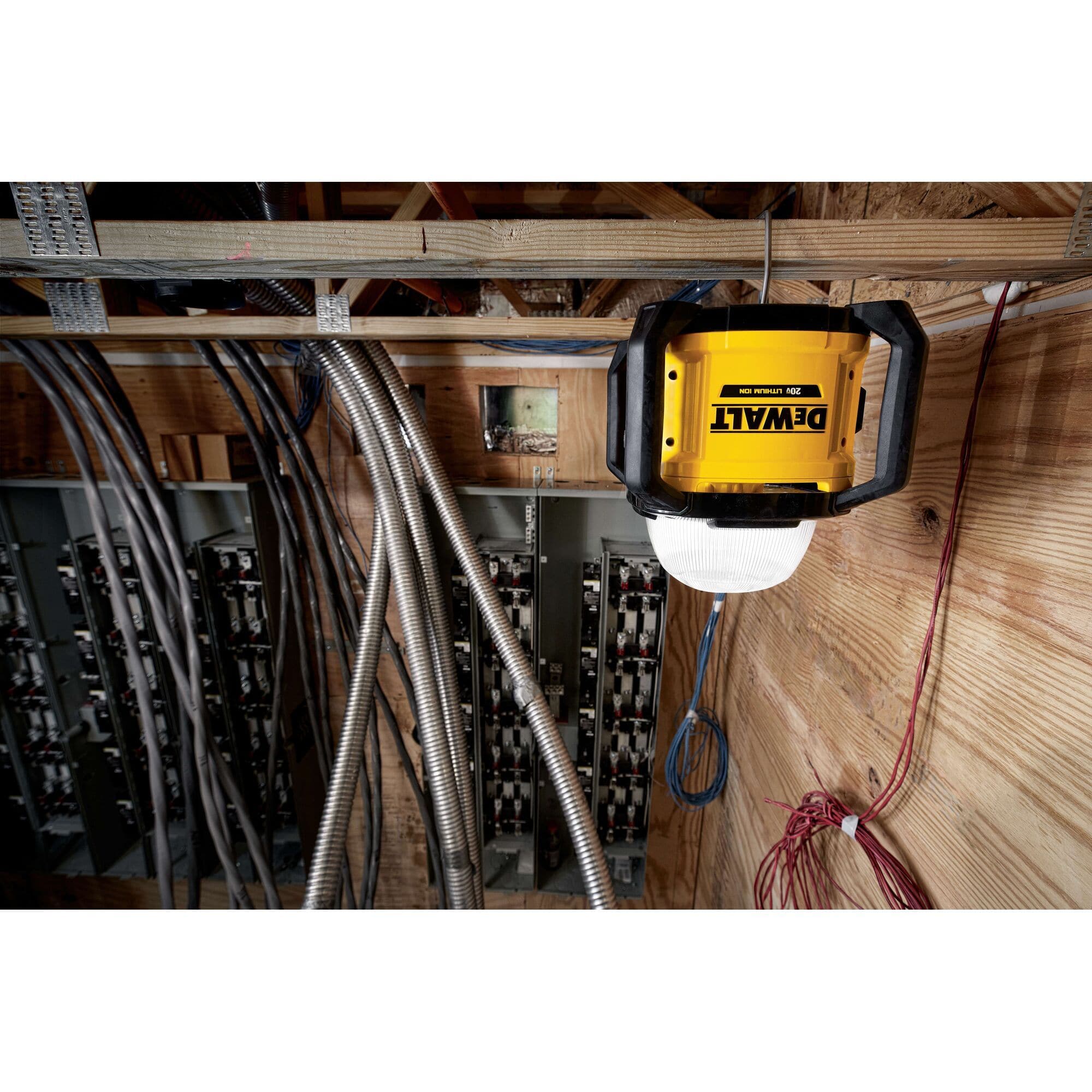 Action shot of the DEWALT cordless area light hanging above an industrial electrical panel, demonstrating its versatility for high-visibility technical inspections and wiring tasks.