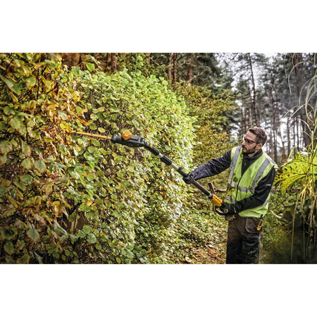A worker on a residential property using the DEWALT 20V MAX pole hedge trimmer to manage dense roadside foliage, showcasing the tool's balance and 2,800 SPM cutting speed.
