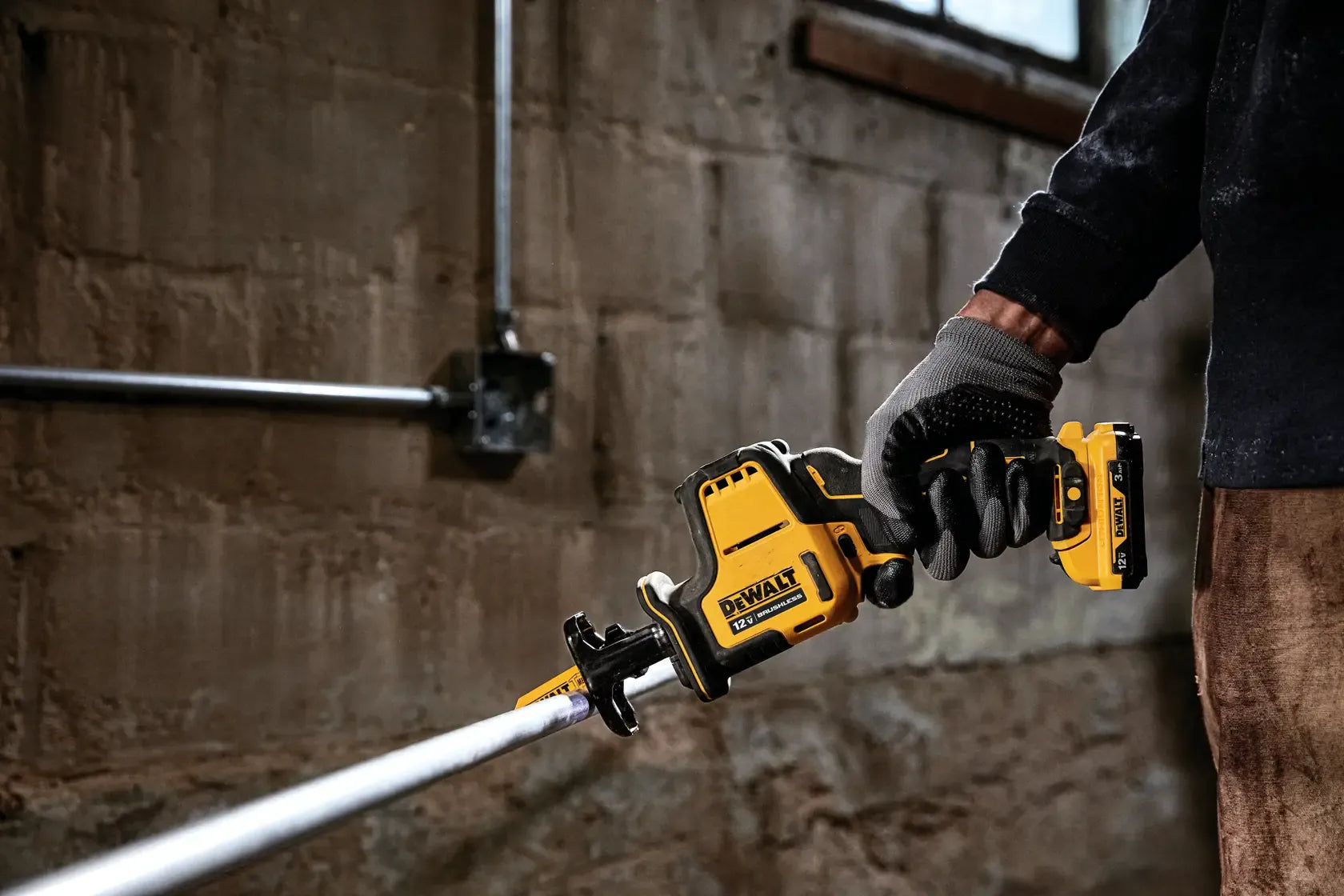 Action shot of an electrician using the DEWALT XTREME 12V MAX one-handed reciprocating saw to cut metal conduit in a dim industrial workspace.