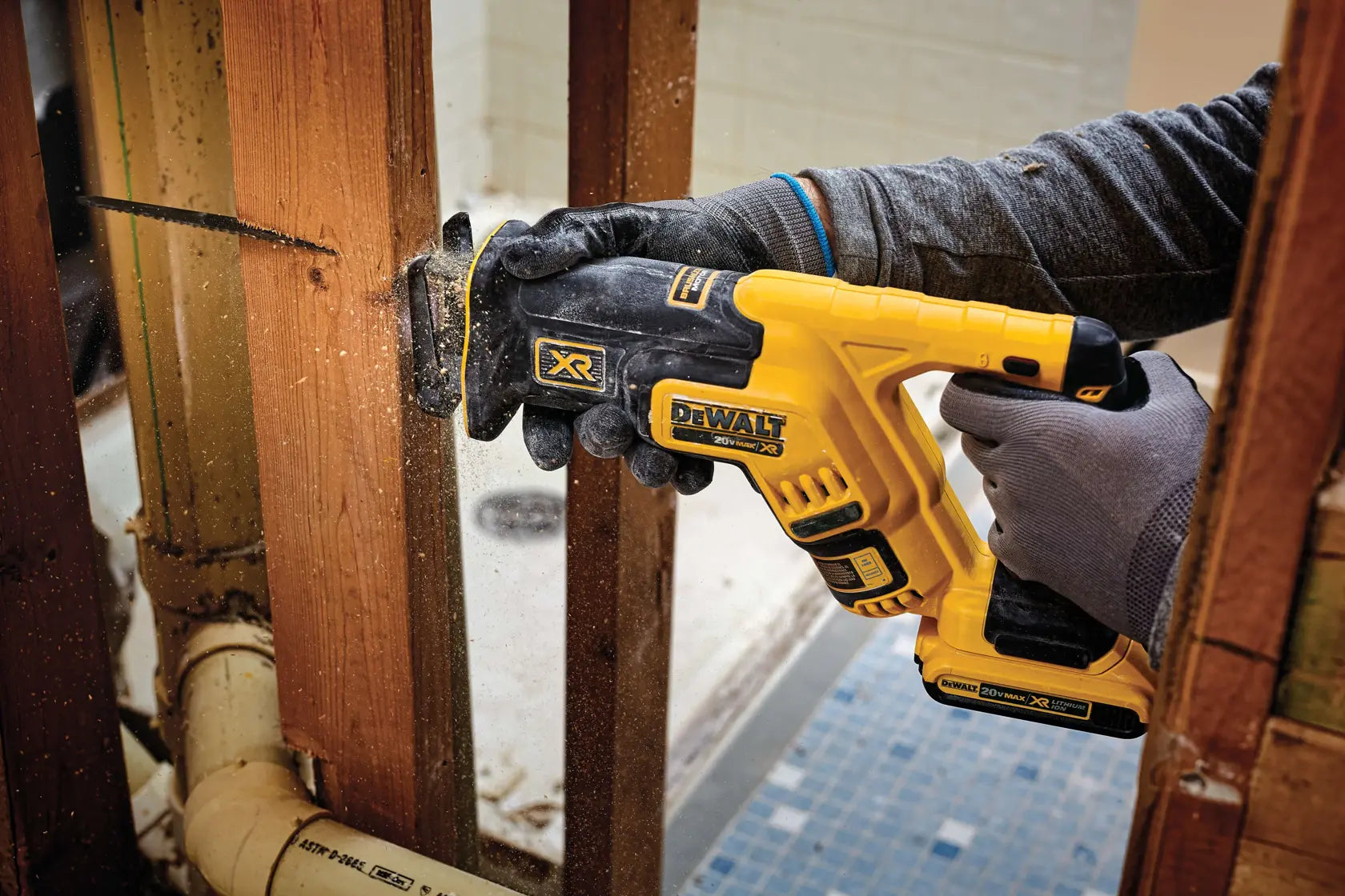 A close-up action shot of the DEWALT 20V MAX XR compact reciprocating saw cutting through a vertical wooden stud. The image captures sawdust being ejected, highlighting the 1-1/8 inch stroke length and the efficiency of the brushless motor during framing and demolition work.