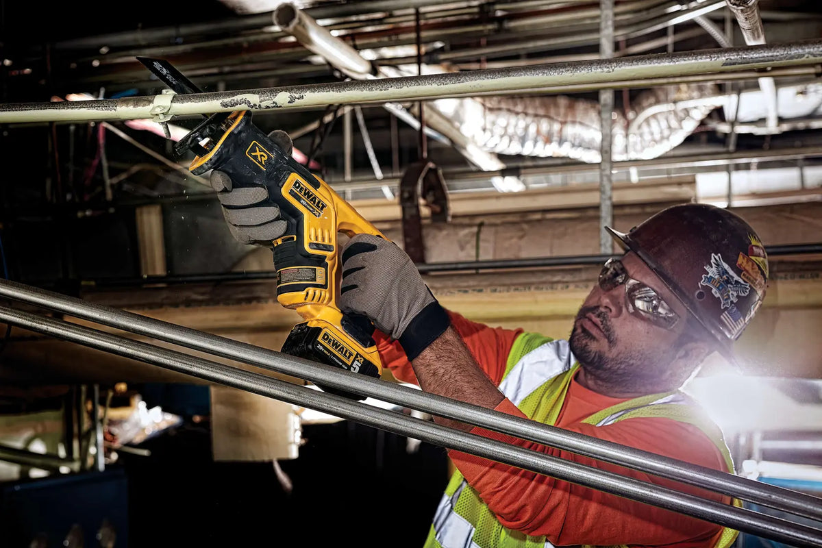 A professional plumber using the DEWALT compact reciprocating saw to cut overhead metal piping. The image highlights the tool's lightweight balance and cordless freedom, making it an essential device for mechanical contractors and facility maintenance.