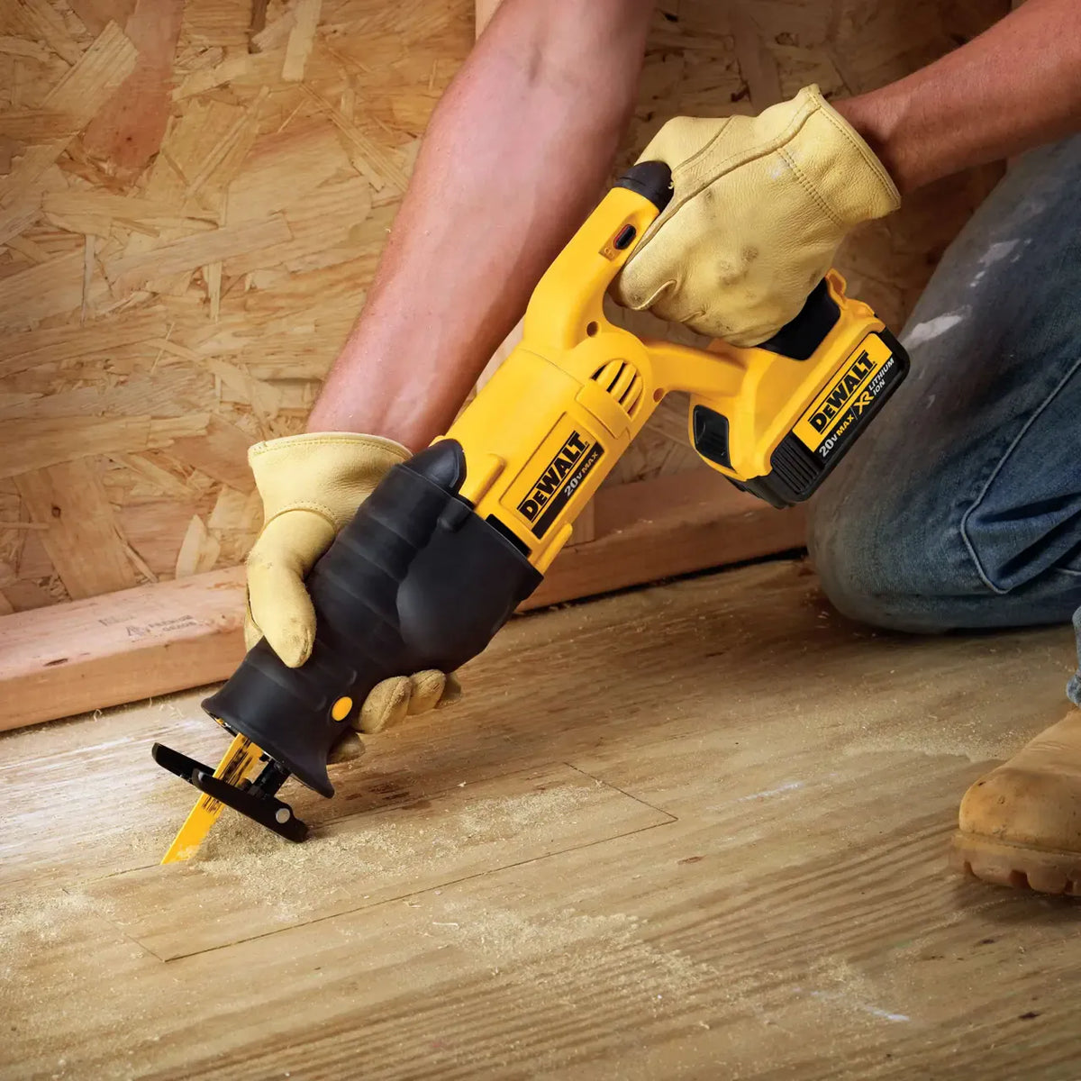 A contractor wearing thick leather safety work gloves kneeling down to make a precision plunge cut into structural plywood subfloor panels using the DEWALT twenty volt max cordless reciprocating saw.