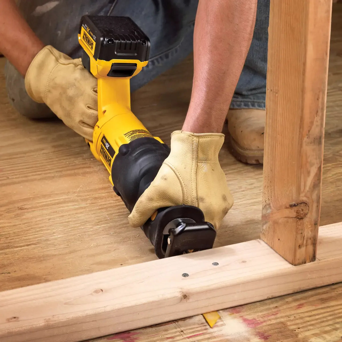 Close up detail shot of a professional craftsman using a DEWALT cordless reciprocating saw fitted with a yellow cutting blade to cut smoothly through a wooden two by four framing stud on a residential job site.