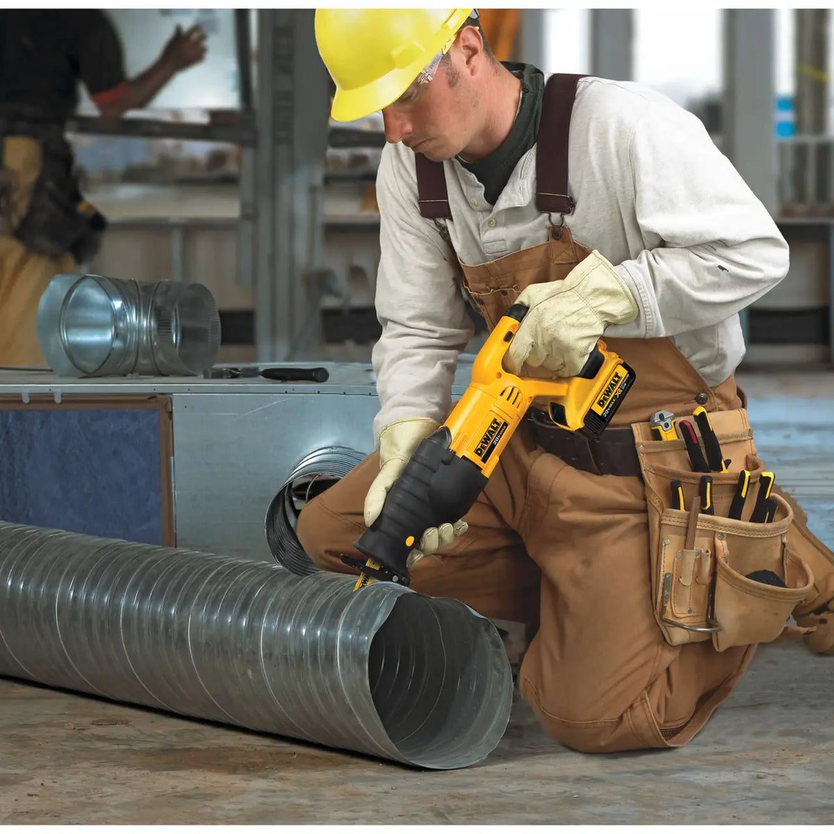 An HVAC installation technician wearing a yellow safety hard hat, protective glasses, and leather work gloves kneeling down to cut a large corrugated metal ventilation duct utilizing the DEWALT cordless reciprocating saw.