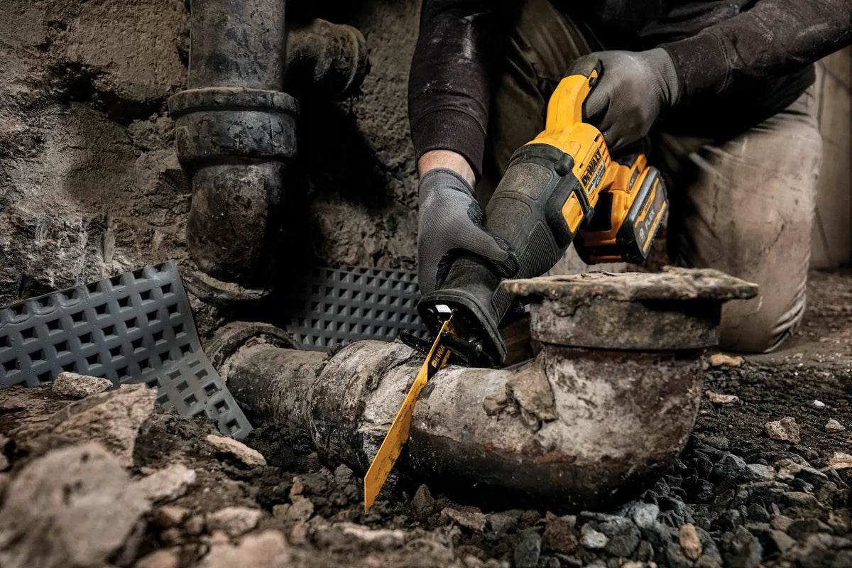 Close-up action photograph of the DCS389 reciprocating saw in use, cutting through a heavy-gauge rusted metal pipe. The image illustrates the high-torque demolition power of the brushless motor and the efficiency of the specialized metal cutting blade.