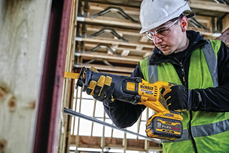 An action lifestyle shot of a construction worker using the DEWALT 60V MAX saw to cut through structural steel and wood framing. The technician is wearing a hard hat and safety glasses, emphasizing the tool's use for high-performance commercial construction and demolition.