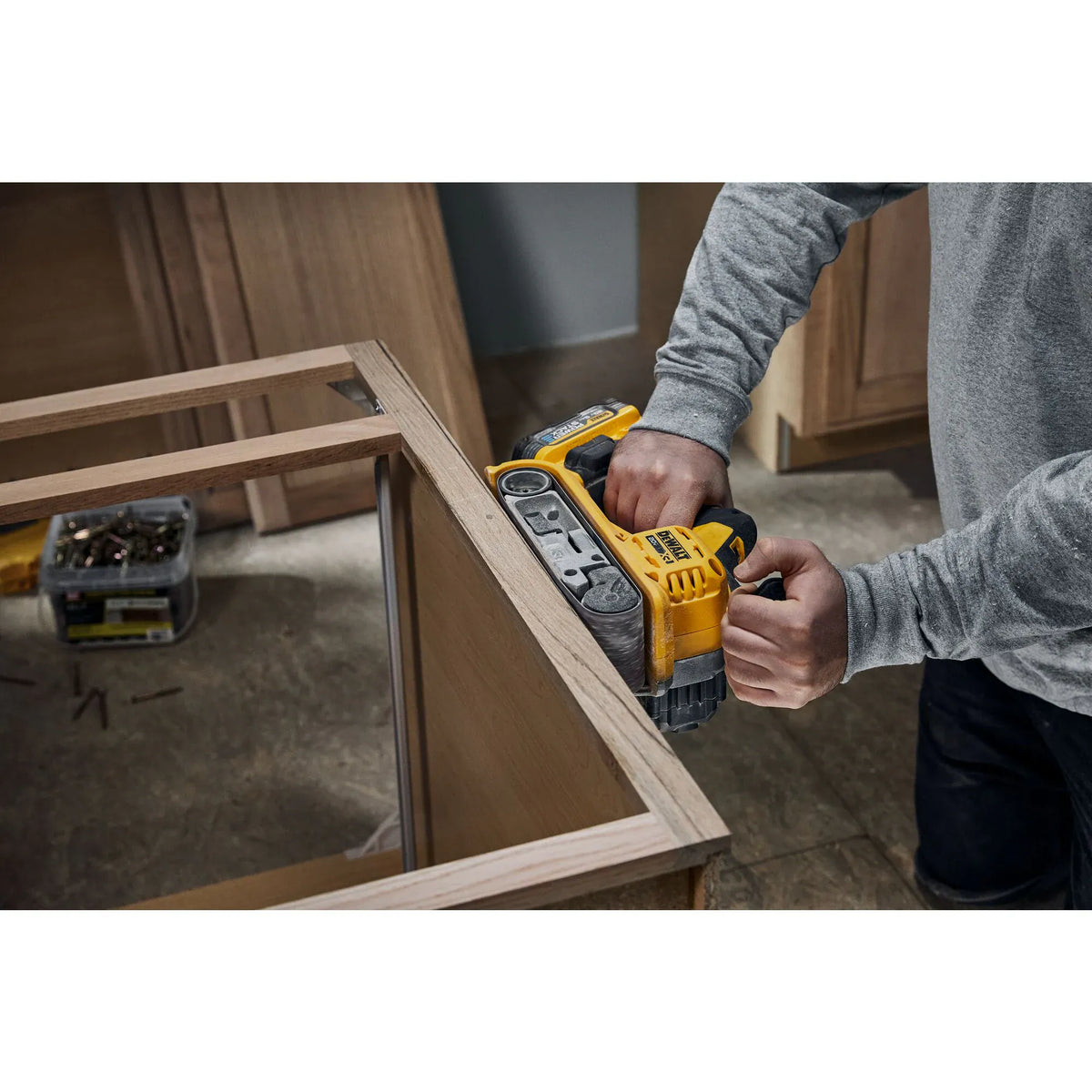 Action shot showing a technician using the DEWALT cordless belt sander to scribe and smooth the edge of a cabinet frame. The image illustrates the tool's balance and the benefit of the over-molded grip during detailed vertical sanding applications.