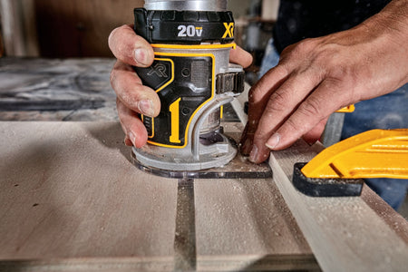An operational close-up view of a craftsman guiding the 20V compact cordless router along a template guide line secured to a piece of premium lumber, demonstrating stable fixed-base tracking and clear bit visibility.