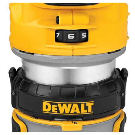 A close-up studio shot of the upper section of the DEWALT compact wood router, focusing on the yellow housing assembly, black variable speed selector wheel showcasing numbers 5, 6, and 7, and the black ratcheting depth adjustment ring.