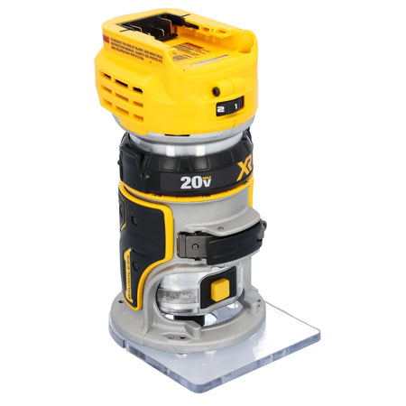 A three-quarter profile studio view of the cordless 1/4-inch router on a white background, highlighting its black textured rubber grip panel, yellow motor lock release button, and clear square fixed base.