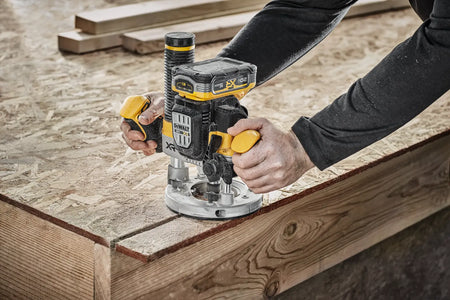Top-down action view of a carpenter operating the DEWALT 20V MAX XR brushless plunge router to cut a precise groove into a sheet of OSB subflooring at a construction jobsite.