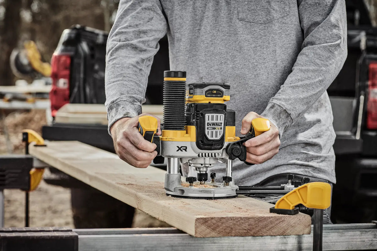 Carpenter using the DEWALT DCW620B 20V MAX XR cordless plunge router to edge-trim a thick piece of dimensional lumber, demonstrating the tool's portability and power in an outdoor work setting.