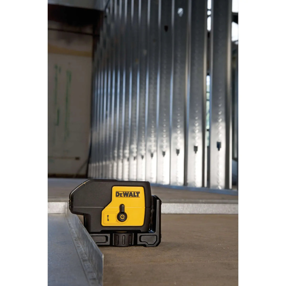DEWALT DW083K spot laser pointer level sitting on a concrete floor next to a bottom metal track, aligned perfectly to lay out a long wall of steel studs in a commercial building.