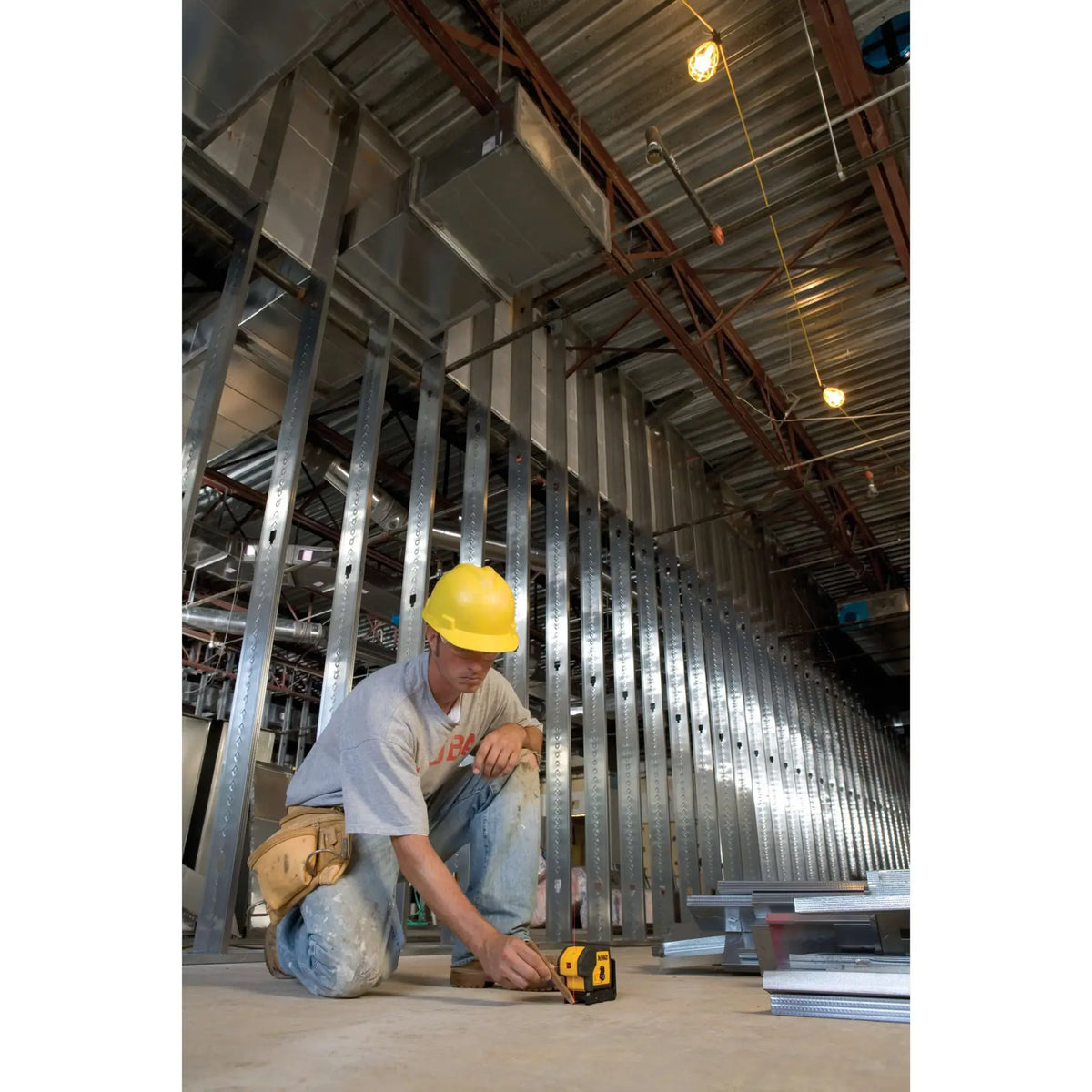 Professional contractor wearing a hard hat on a commercial job site using the DEWALT DW083K 3-beam laser pointer to precisely lay out a long metal track wall.