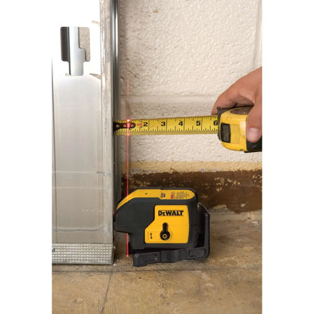 Close-up of a worker using a yellow tape measure to verify the exact distance from a metal stud to the highly visible red laser beam emitted by the DEWALT DW083K.