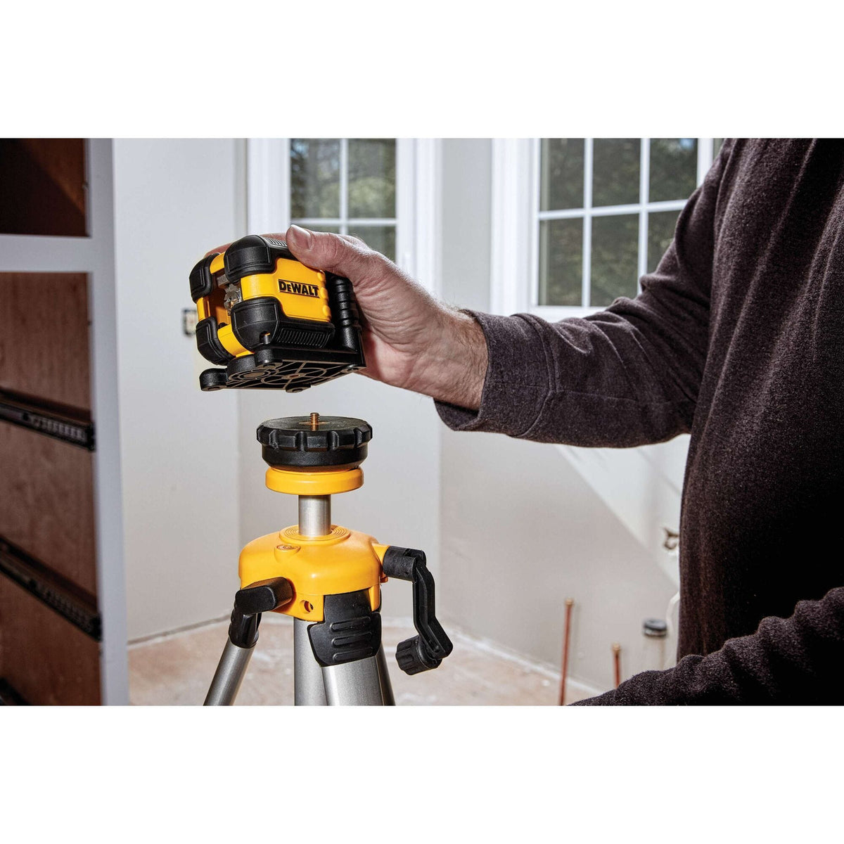 A contractor installing the DEWALT DW08802 Red Cross Line Laser onto a 1/4-inch threaded tripod mount, demonstrating the tool's ease of setup for professional leveling and alignment in interior remodeling.