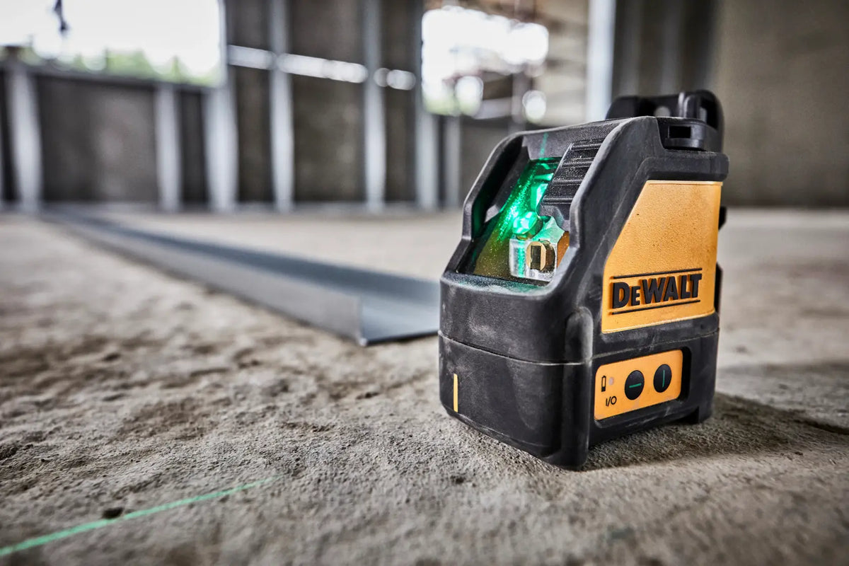 Close-up action shot of the DEWALT DW088CG self-leveling laser resting on a concrete slab, projecting a bright green horizontal guide line across the floor for precise construction layout.