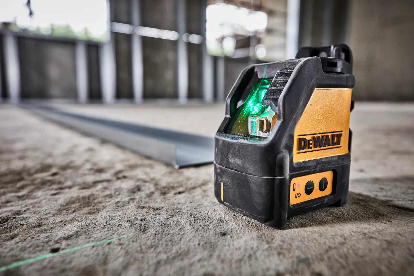 Close-up action shot of the DEWALT DW088CG self-leveling laser resting on a concrete slab, projecting a bright green horizontal guide line across the floor for precise construction layout.