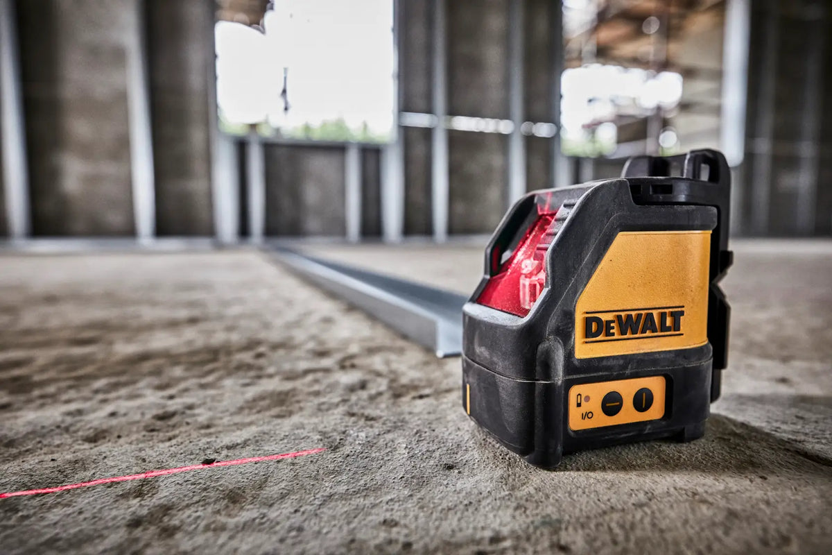 A low-angle action shot of the DEWALT red beam laser level sitting on a concrete subfloor. The unit is projecting a sharp red vertical line onto a metal track, demonstrating the tool's self-leveling capabilities for accurate commercial layout and installation.
