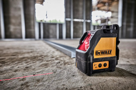A low-angle action shot of the DEWALT red beam laser level sitting on a concrete subfloor. The unit is projecting a sharp red vertical line onto a metal track, demonstrating the tool's self-leveling capabilities for accurate commercial layout and installation.