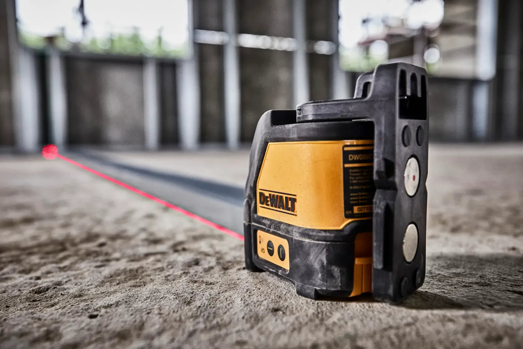 A perspective view of the DW088K laser unit in operation on a construction site. The shot emphasizes the rugged over-molding and the magnetic pivot bracket as the unit projects a long, bright red laser line across a concrete floor for floor-to-ceiling alignment.
